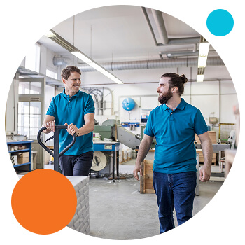 Photo of 2 men in a warehouse setting smiling at each other